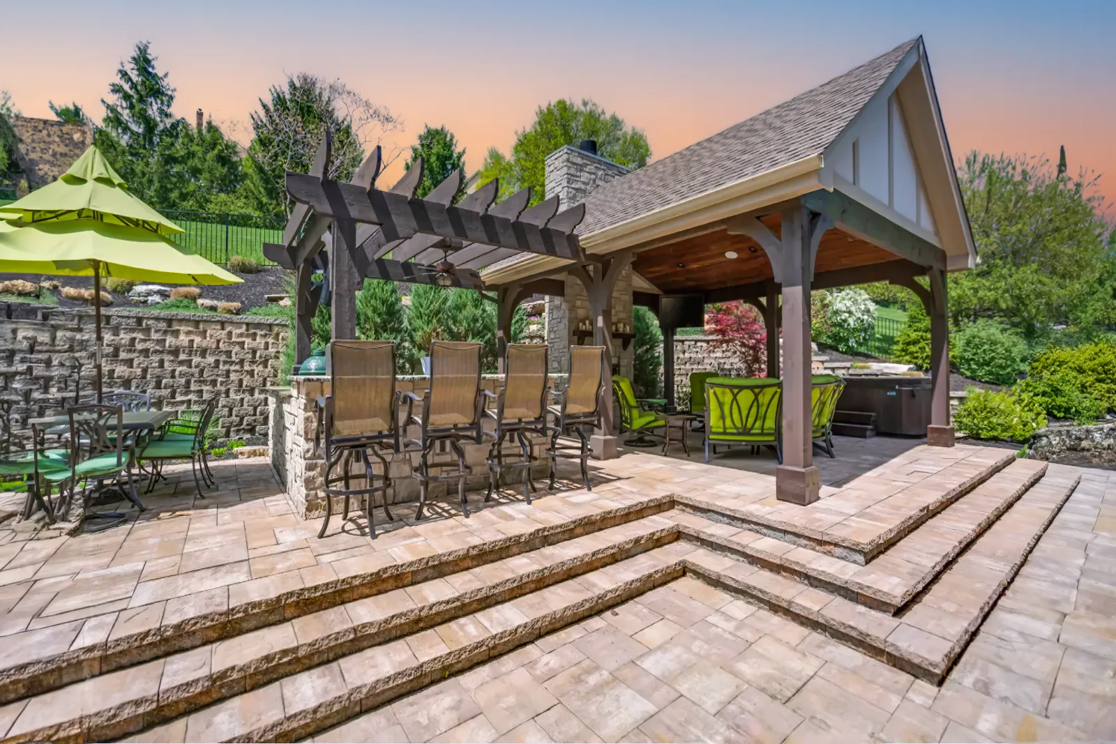 A modern stone patio with a pergola and awning in a residential outdoor space. | Bayside Pavers